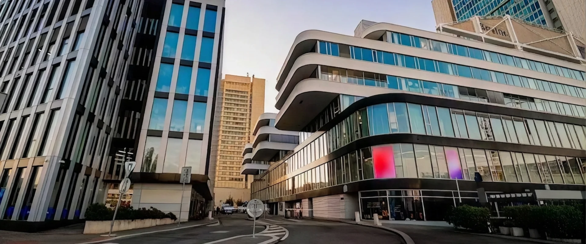 Cubex Centrum Prague seen from the street at dusk — a curved white and glass building, with the office towers of Pankrác alongside it.